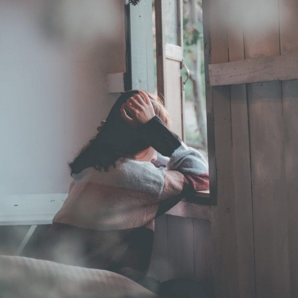 Teen holding head leaning against a window