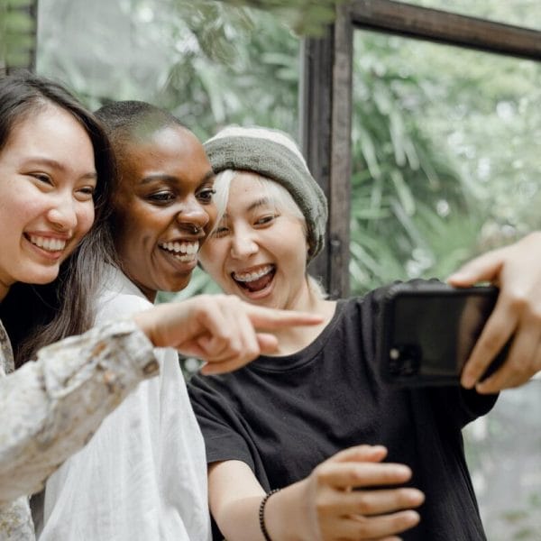 Three teen girls pointing at a mobile phone.