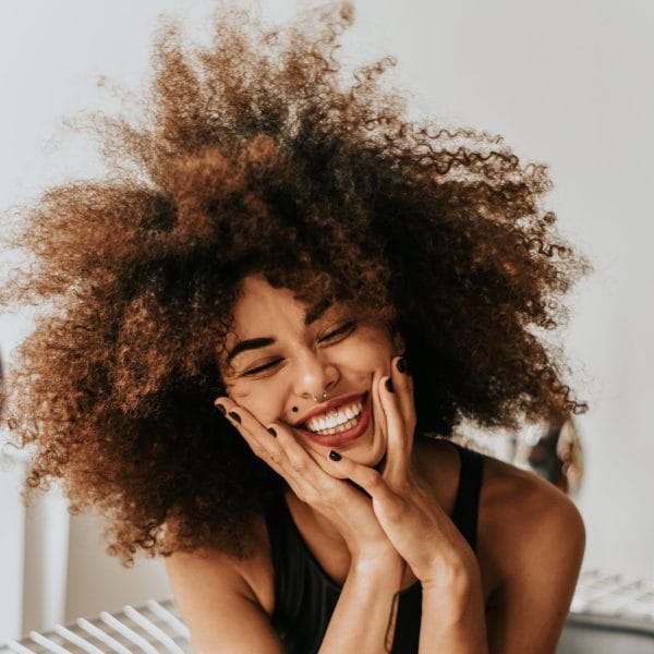 A photo of a woman smiling and holding her hands to her cheeks