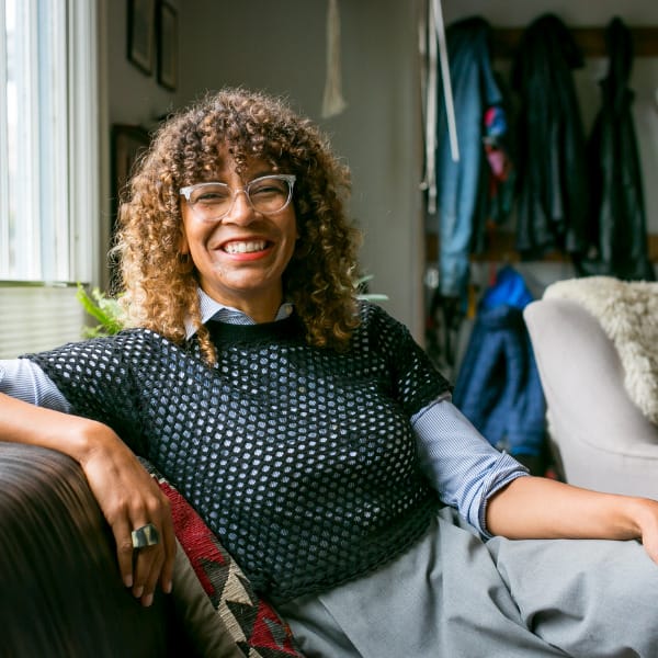 Julie Tinker sits on a couch looking at the camera with her arm propped on up