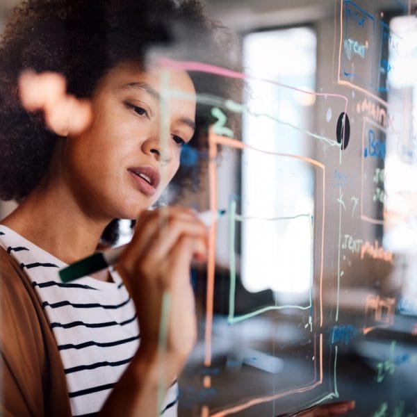 A young woman drawing a diagram and making notes on a glass board