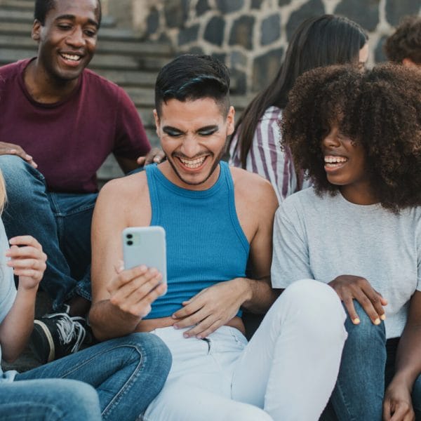 A diverse group of people having fun looking at a cell phone.