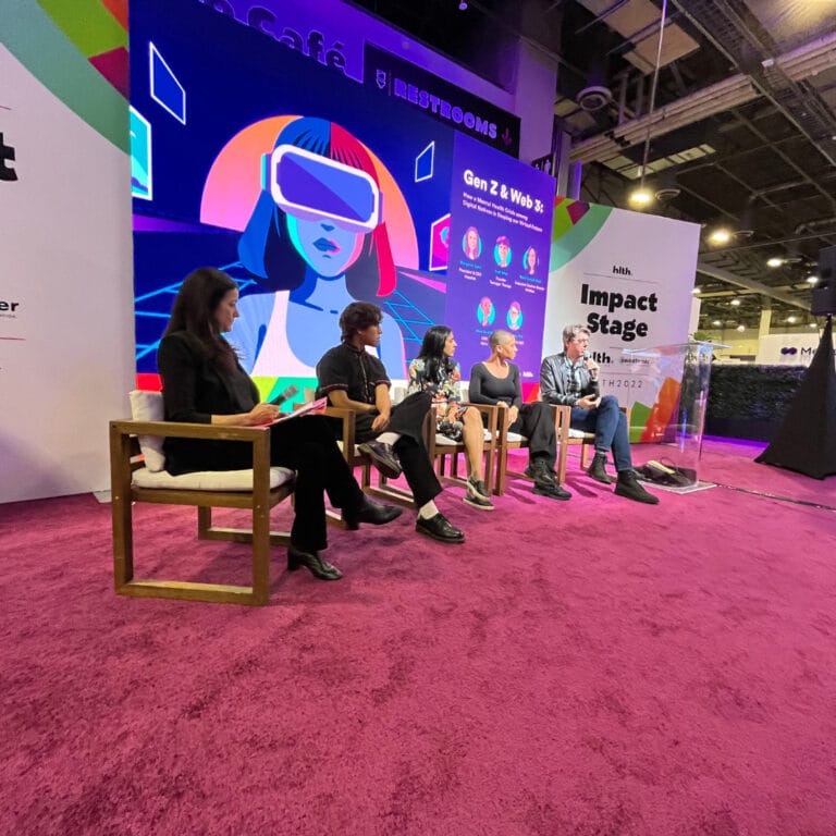 HLTH panelists on stage with red carpet and purple background 